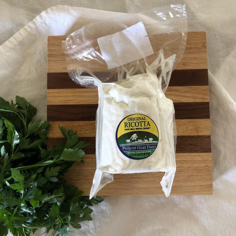 Packaged ricotta cheese from Philpott Goat Dairy on a wooden cutting board with parsley.
