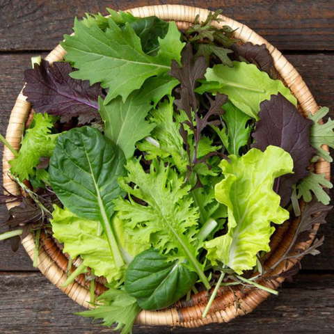 Basket of mixed green leafy vegetables on a wooden surface